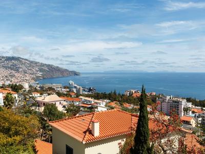 Vista de una ciudad costera con techos rojos y cielo azul sobre el mar.