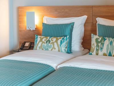 Dos camas individuales con mantas turquesas y cojines estampados en una habitación de hotel.