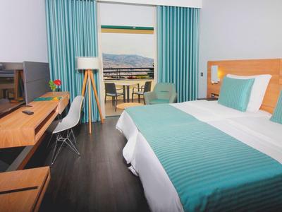 Habitación de hotel moderna con cama doble, escritorio, televisor y balcón con vistas.