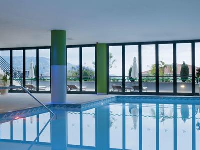 Piscina interior con grandes ventanales, columnas verdes y vista al exterior y montañas.