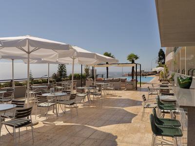 Terraza con sillas y mesas, sombrillas y vista al mar en un día soleado.