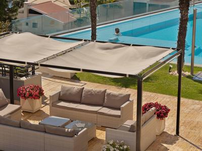 Acogedora zona de descanso al aire libre con sofá y toldos junto a una piscina azul del hotel.