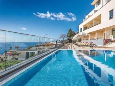 Piscina al aire libre junto a un hotel con vistas al mar y cielo despejado.