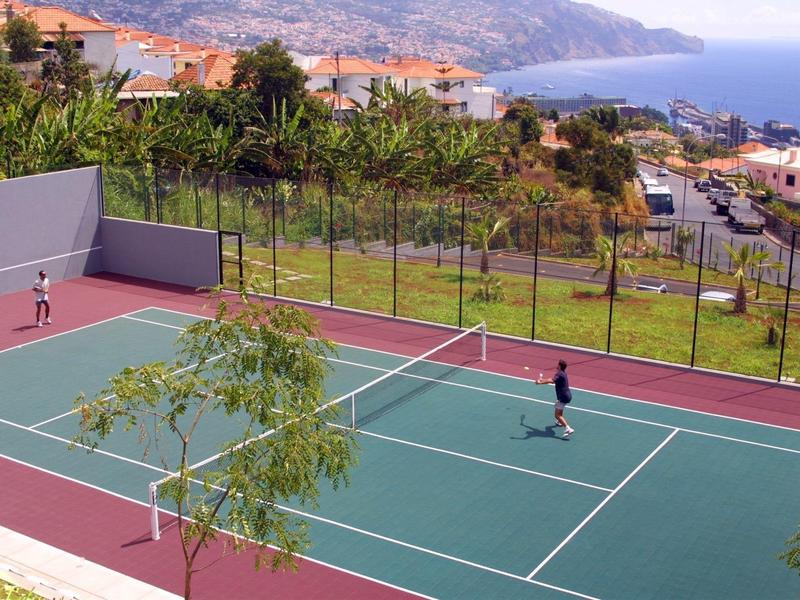Dos personas jugando tenis en una pista con vistas al mar y montañas.