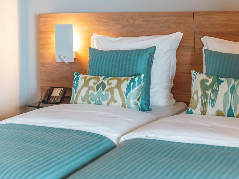 Dos camas individuales con mantas turquesas y cojines estampados en una habitación de hotel.