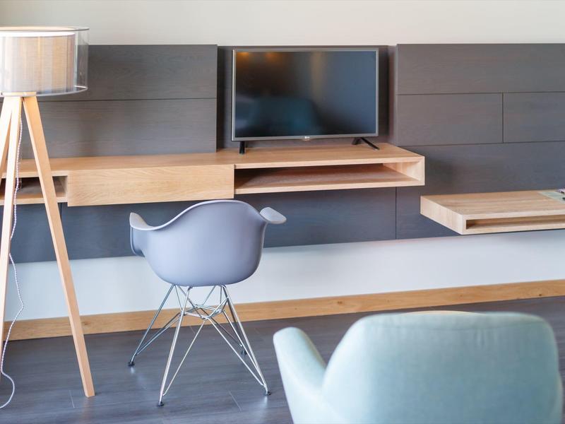Espacio de trabajo moderno con escritorio, silla, lámpara de pie y televisor en tonos neutros.