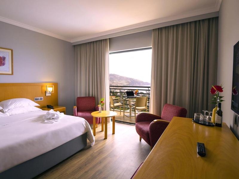 Habitación de hotel moderna con cama doble, balcón y vista a las montañas durante el día.