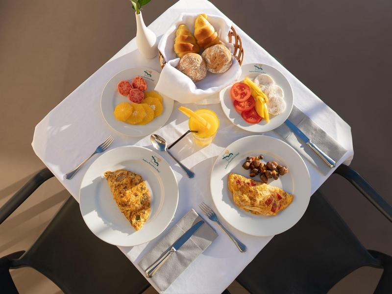 Diversos platos de desayuno sobre una mesa blanca con pasteles, frutas y huevos.