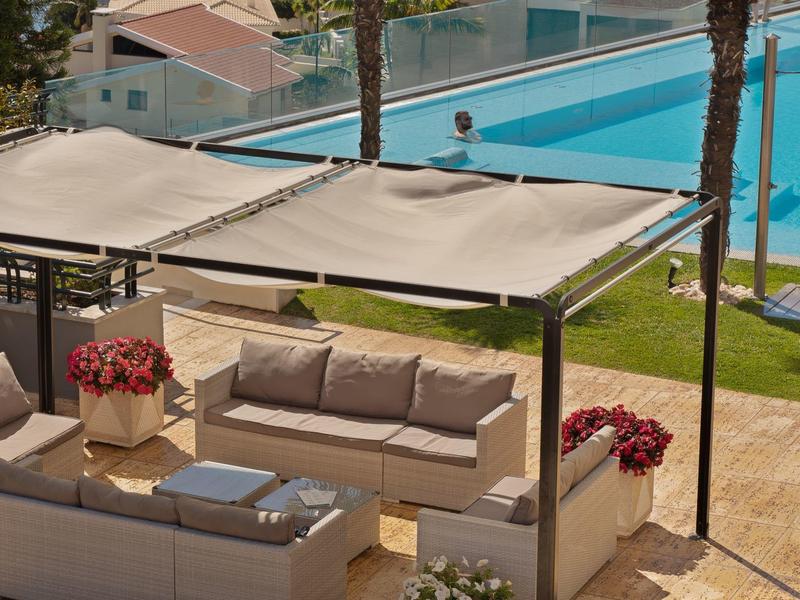 Acogedora zona de descanso al aire libre con sofá y toldos junto a una piscina azul del hotel.