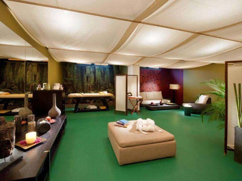 Habitación de hotel espaciosa y luminosa con alfombra verde, muebles y iluminación decorativa.