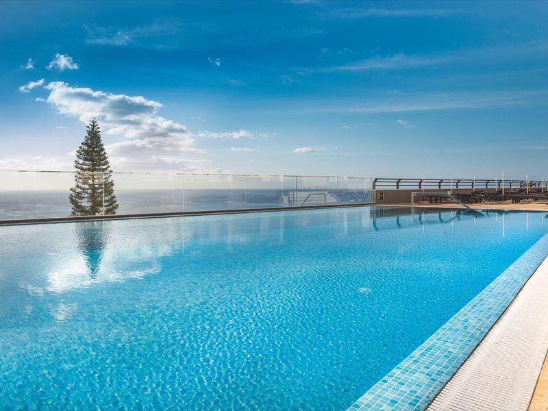Piscina infinita con agua azul clara y vista al océano bajo un cielo nublado.
