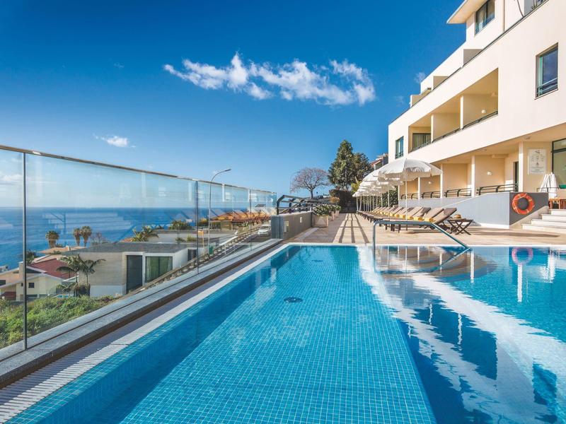 Piscina al aire libre junto a un hotel con vistas al mar y cielo despejado.