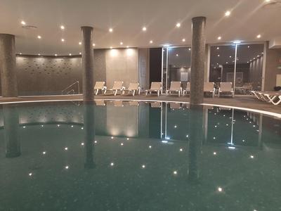 Vnitřní bazénová oblast se sloupy, lehátky a tlumeným osvětlením.