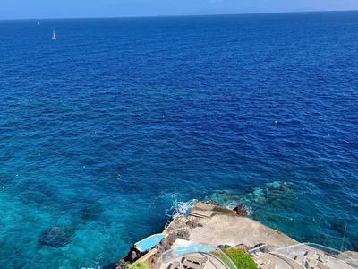 Výhled na čisté modré moře s pobřežní skalou a schody vedoucími k vodě.