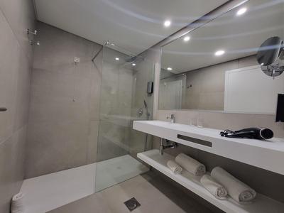 Moderní koupelna s velkým skleněným sprchovým koutem a bílými ručníky na otevřené polici.