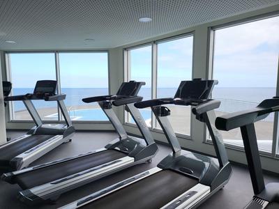 Fitnessraum mit Laufbändern und großen Fenstern mit Meerblick.