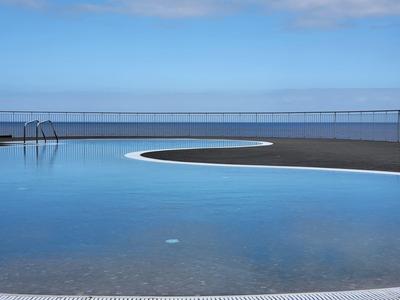 Kulatý venkovní bazén s čistou modrou vodou pod modrou oblohou a zábradlím v pozadí.