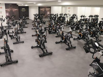 Großer Fitnessraum mit vielen stationären Fahrrädern auf grauem Boden.