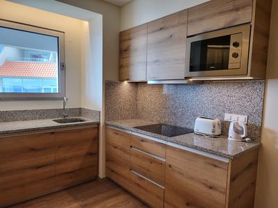 Moderní kuchyně s dřevěnými předními deskami, mozaikovými obklady a spotřebiči jako mikrovlnná trouba, toustovač a varná deska.