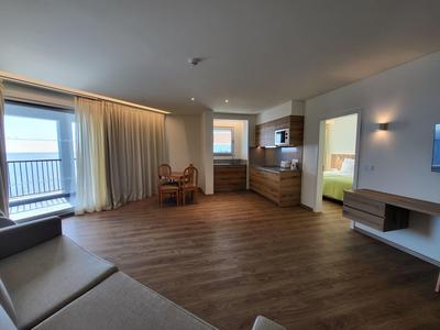 Světý hotelový pokoj s kuchyňským koutem, jídelním stolem a balkonem s výhledem na moře.