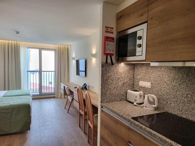 Moderní hotelový pokoj s kuchyňským koutem, jídelním stolem a balkonem s přirozeným světlem.