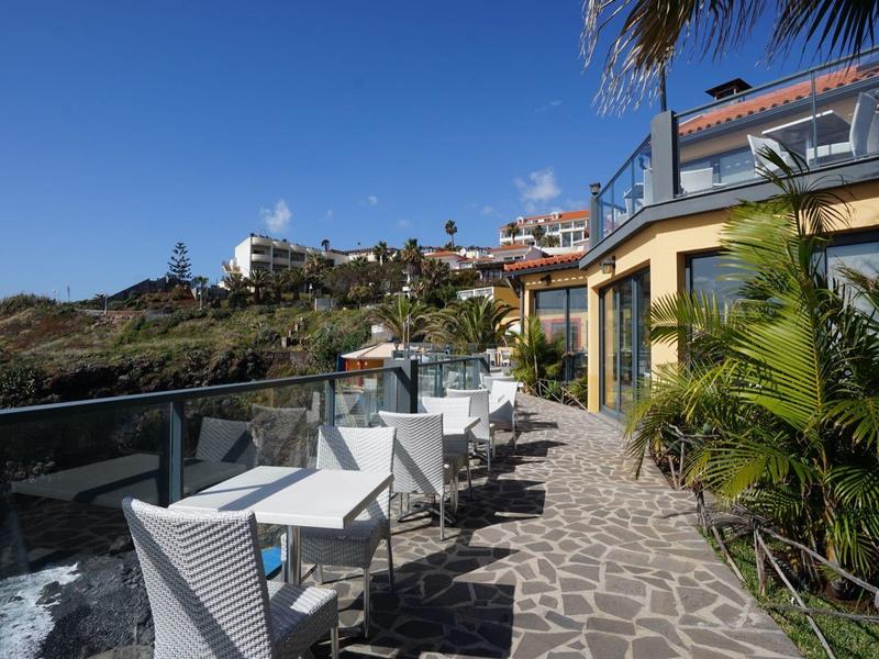 Terasa s bílými židlemi a stoly za slunečného dne s výhledem na moře.