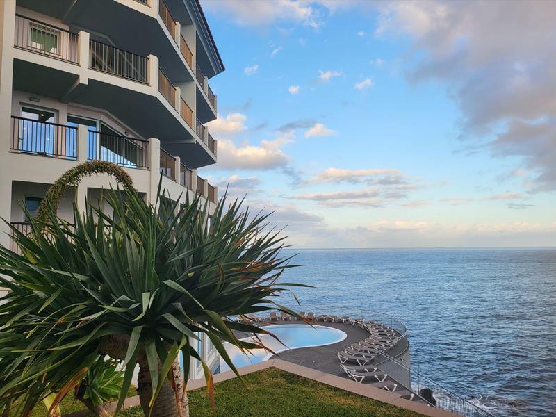 Pohled na pobřežní promenádu se zelení a vícepodlažní budovou pod jasnou oblohou.