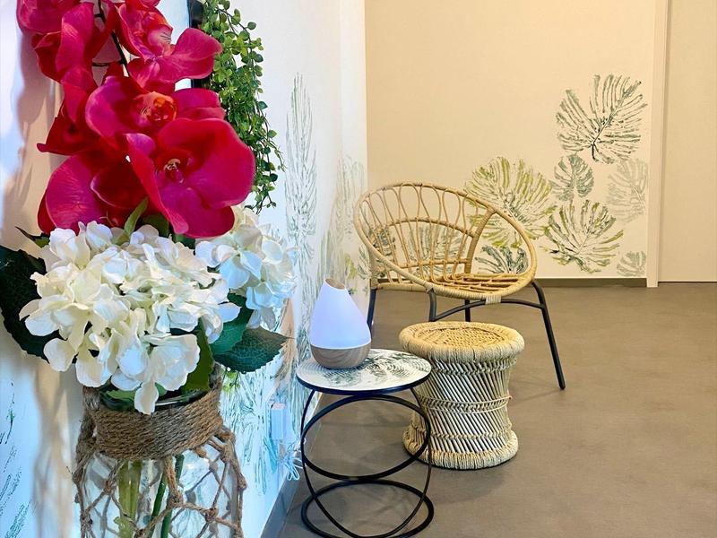 Chodba s dekorativními květinovými aranžmá a ratanovým nábytkem na bílé stěně.