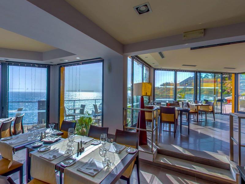 Světla restaurace s velkými okny s výhledem na moře a hory za denního světla.