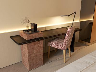 Moderner Schreibtisch mit schwarzer Glasplatte und gemustertem Stuhl in einem Hotelzimmer.