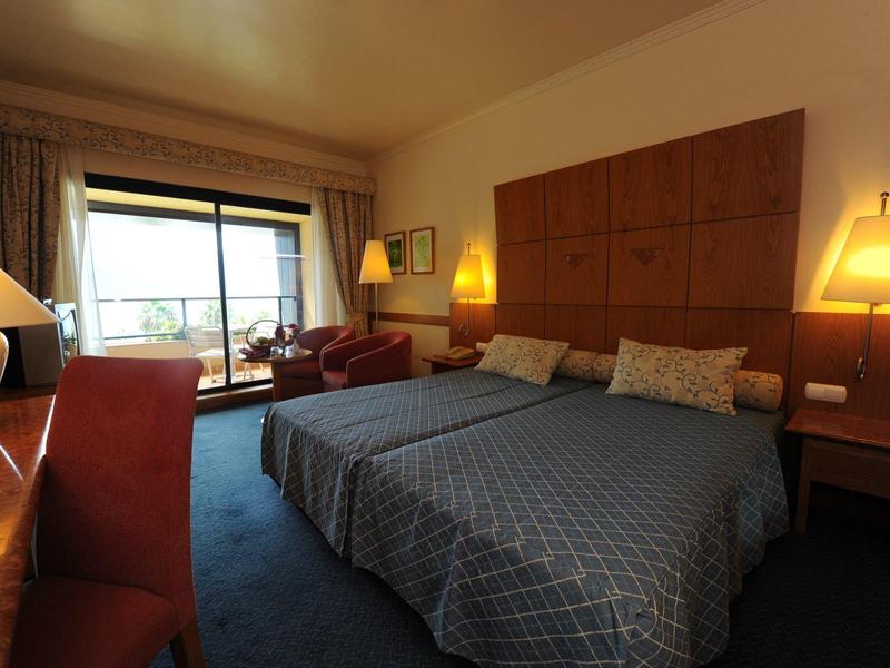 Cozy hotel room with two beds, armchairs, and view of a balcony.