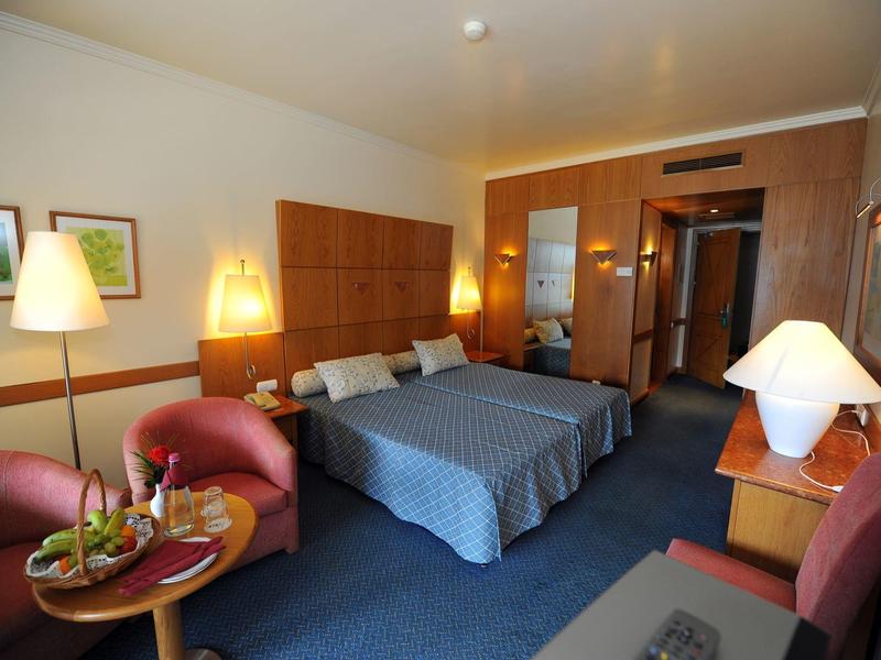 Hotel room with double bed, two armchairs, nightstands, and warm lighting.