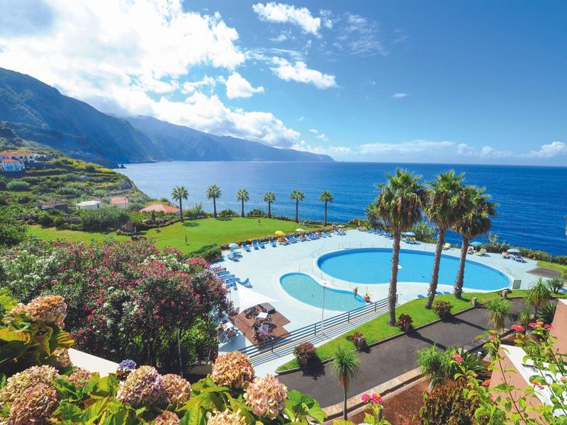 View of a pool with palm trees and ocean under a partly cloudy sky at a resort.
