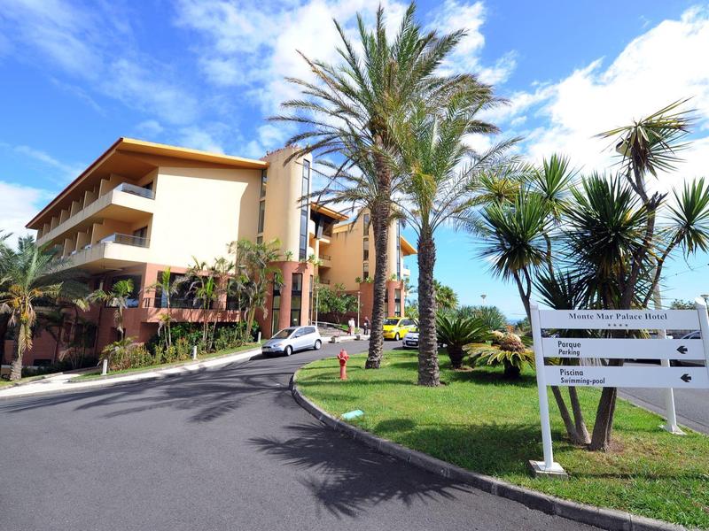 Hotel building with balconies, surrounded by palm trees and blue sky.