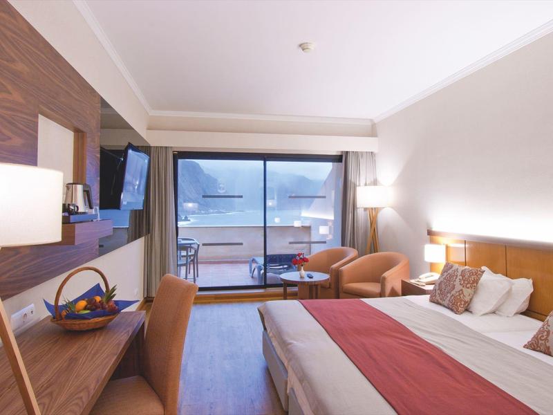 Modern hotel room with double bed, desk, balcony, and water view.