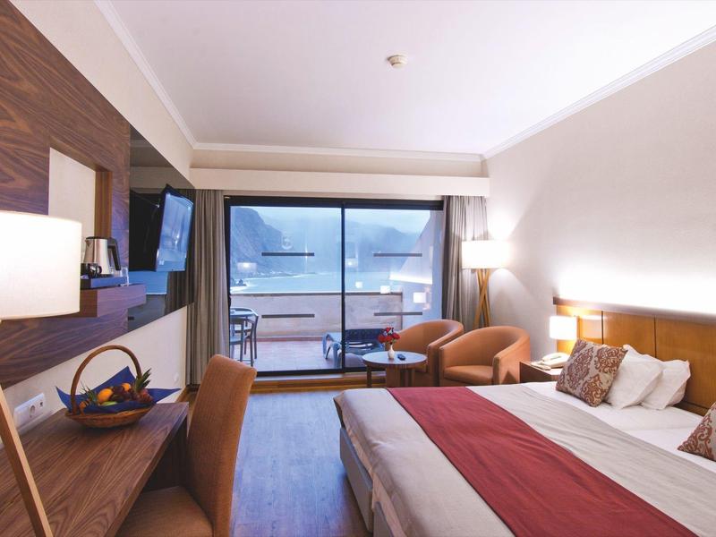 Modern hotel room with large bed, balcony, and view of mountains and lake.