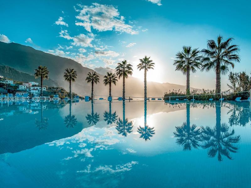 Palm trees reflect calmly in a pool's water at sunset.