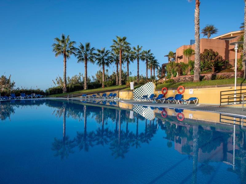 Spacious pool with palm trees and lounge chairs under a clear blue sky.