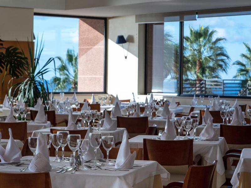 Elegant restaurant with white-set tables and sea view through large windows.