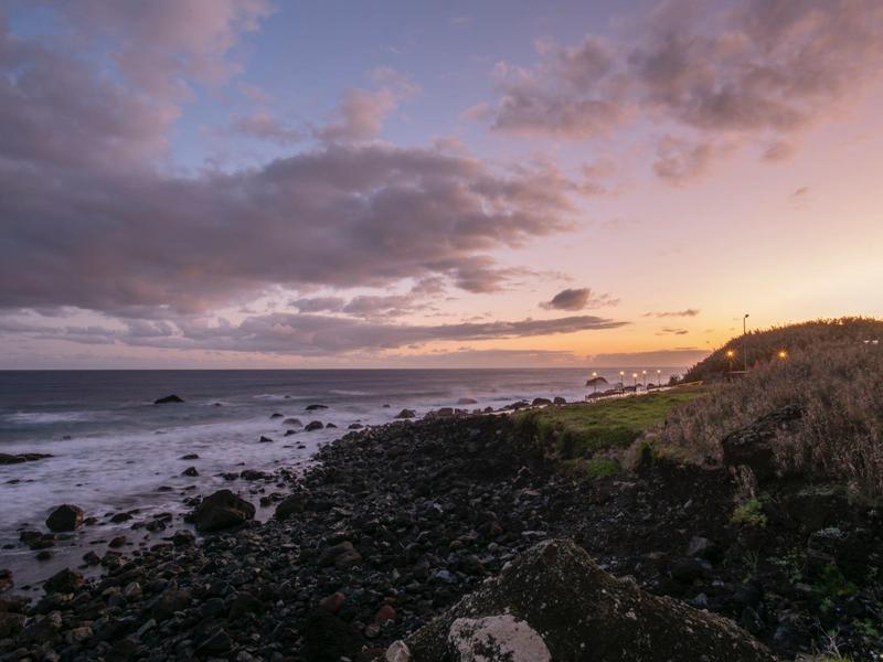 Coastal landscape with rocky shore and cloudy sky at sunset.
