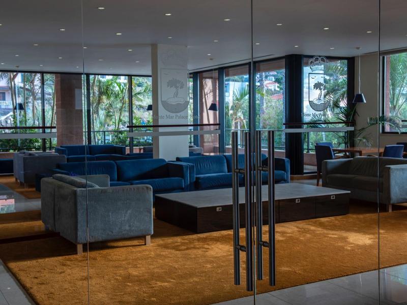 Modern hotel lounge area with blue sofas, glass walls, and an orange carpet.