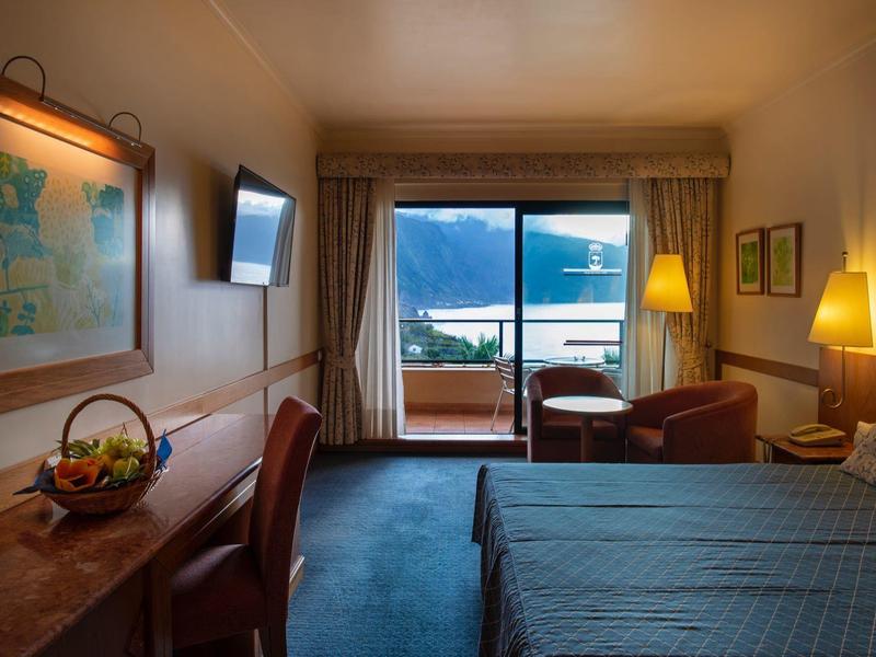 Cozy hotel room with balcony, mountain and lake view, desk, and double bed.