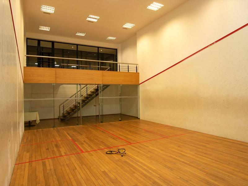 Modern squash court with wooden floor and glass wall in bright room.