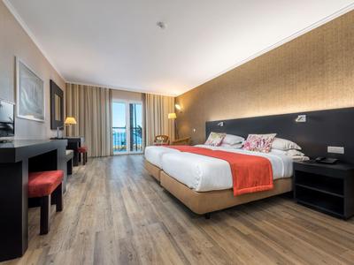 Modernes Hotelzimmer mit großem Bett, Holzboden, Schreibtisch und Balkon mit Meerblick.