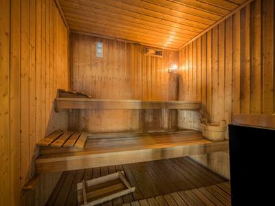 Holzsauna mit mehrstufigen Bänken, Holzboden, Eimer und Kelle, warmes Licht, Dampf in der Luft.