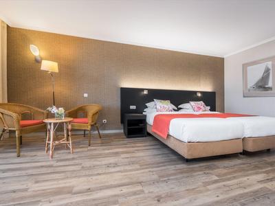 Modernes Schlafzimmer mit Doppelbett, Holzboden, zwei Stühlen und warmen Wänden.