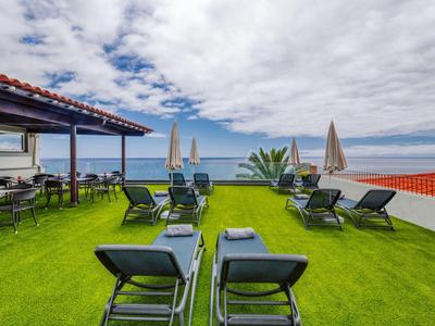 Terrasse mit grüner Rasenfläche, Liegestühlen, Sonnenschirmen und Meerblick unter wolkigem Himmel.