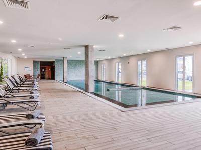 Moderner Innenpool mit großen Fenstern, Holzfliesenboden und mehreren Liegen an der Seite.