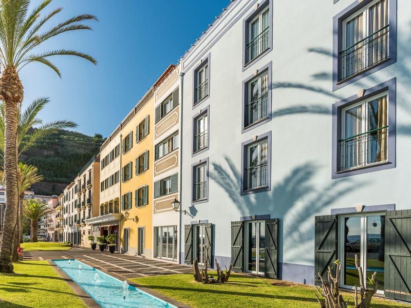 Multi-story hotel building with swimming pool and palm trees in front of a mountain