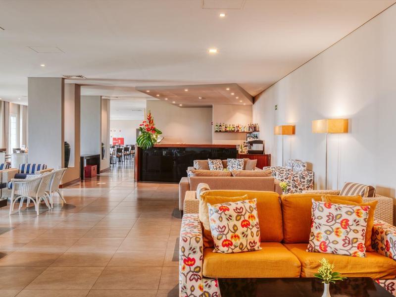 Bright lobby with yellow sofas, floral patterns, and a reception desk in the background.
